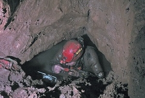 A British cave diver preparing to dive in a tight, muddy sump